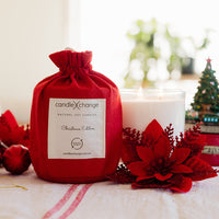 Red candle with 'candlexchange' label surrounded by Christmas decorations on a table.