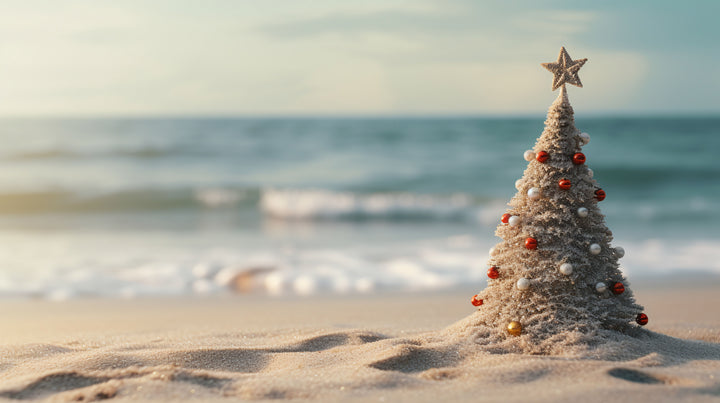 Small Christmas tree with ornaments on a sandy beach with ocean in the background