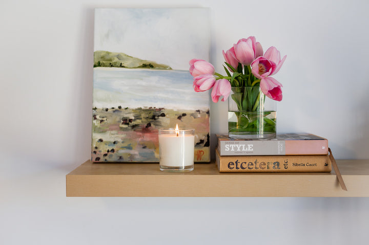 Candle on shelf with flowers and books